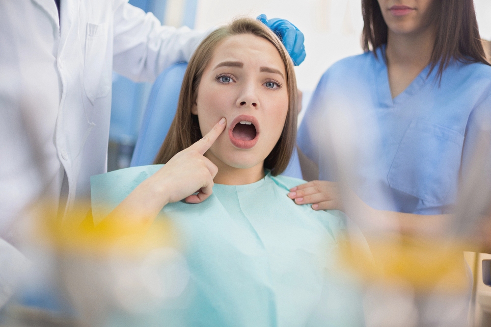 Girl sitting in a dental chair pointing to her teeth while speaking to a dentist - Overbite vs Underbite in Rocky Point, NY.