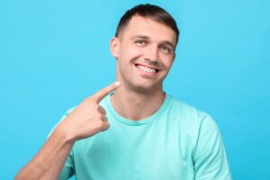 smiling man pointing his metal braces - Invisalign vs Braces Cost in Rocky Point, NY